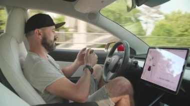 Kyiv, Ukrayna. Ağustos 2021. Adam Tesla 'sında akıllı telefon kullanırken, otomatik pilot otoyol boyunca araba kullanıyor. Otomatik sistem aracın tüm kontrolünü ele geçirebilir. Yüksek kalite 4k görüntü