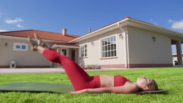 ヨガマットに横になって腰や小便を訓練しながら女性アスリート 女性は裏庭の頭の上に足を持ち上げる 高品質4K映像 — ストック動画