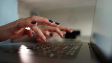 Manikürlü kadın ellerinin evdeki bir odada deftere yazı yazması. Siyah klavye, lenste beyaz ekran. Arka planda ışık odası var. Yüksek kalite 4k görüntü