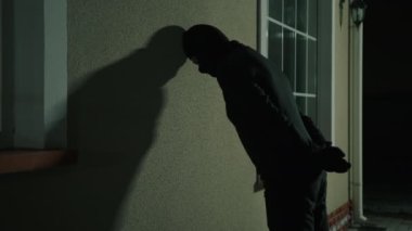 Sahipleri dışarıdayken siyah kar maskeli tanınmayan bir adamın para çaldığı yakın çekim görüntüsü. Yakalanan bir suçlu elleri arkada kelepçelenmeyi bekliyor. Yüksek kalite 4k görüntü
