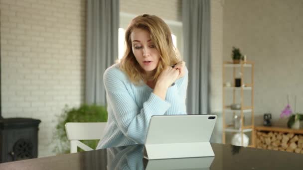 迷人的年轻女性正在家里用白色的平板电脑与舒适的室内环境进行在线对话 金发女郎待人友善 桌子上的石碑 高质量的4K镜头 — 图库视频影像