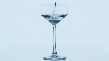Açık gri arka planda ayakta duran bir şarap bardağına temiz su dökülüyor. Su, boş şarap bardağına sorunsuzca akıyor. Yüksek kalite 4k görüntü