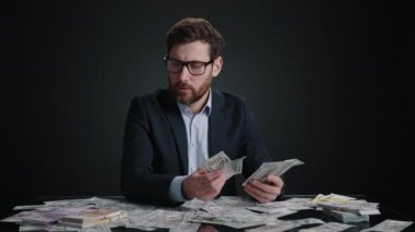 Takım elbiseli ve gözlüklü bir adam para sayıyor ve hayal kırıklığına uğratıyordu. Hayal kırıklığına uğramış görünüyor. Adam siyah odada yatıyor. Yüksek kalite 4k görüntü 