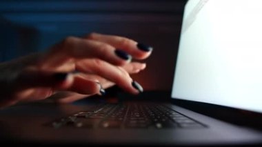 Not defterine yazı yazan, karanlık bir odada bilgi arayan kadınların ellerini kapat. Siyah klavye, objektifte parlak ekran. Parmaklar hızlı basıyor. Yüksek kalite 4k görüntü