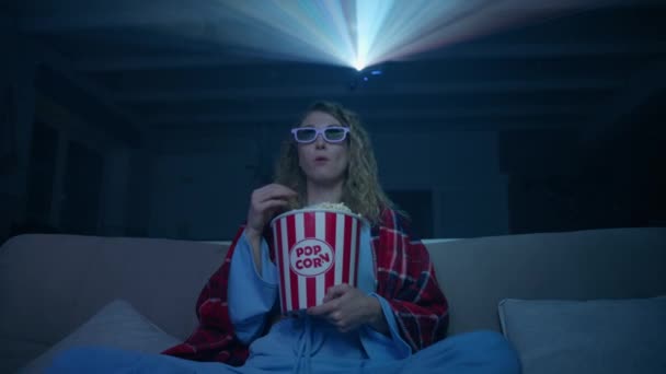 白人妇女穿着3D眼镜看电影 在家里吃爆米花 靠近一个兴奋的年轻女子 一头卷曲的金发 背后的投影仪光束 高质量的4K镜头 — 图库视频影像