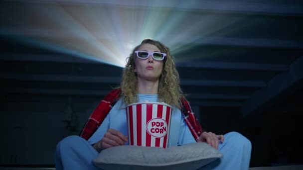 白种人女人穿着带爆米花的3D眼镜看电影 卷曲头发的年轻女人坐在沙发上 投影仪的光束在后面 高质量的4K镜头 — 图库视频影像