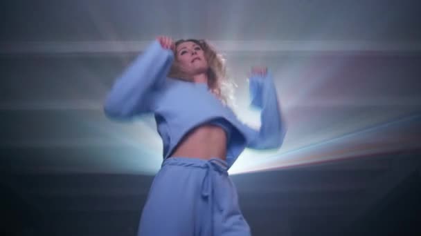 プロジェクターでミュージックビデオを見て 自宅で踊る幸せな若い女性 楽しさを持つ青いスーツのケアフリー女性 プロジェクターは背景にビームします 高品質4K映像 — ストック動画