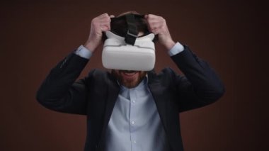 Takım elbiseli bir adam kulaklığını takıyor ve yüzünde mutluluk var. O, basit bir koyu kahverengi arka plandadır. Şaşırmış görünüyor. Yüksek kalite 4k görüntü