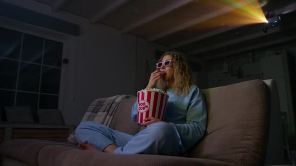ポップコーンで映画を楽しんでいる若い女性 彼女のホームシアターで3D映画を見て白人女性 背景に多色プロジェクタービームと 高品質4K映像 — ストック動画