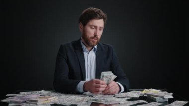 Hayal kırıklığına uğramadan önce takım elbiseli bir adam yığınla para sayıyor. Hayal kırıklığına uğramış görünüyor. Adam siyah odada yatıyor. Yüksek kalite 4k görüntü 