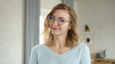 Kameraya flört eden, gözlüklü, gülümseyen genç sarışını yakından çek. Kıvırcık saçlı, mavi kazaklı, alt dudağını üst dişlerinin arasına sıkıştıran bir kadın. Yüksek kalite 4k görüntü