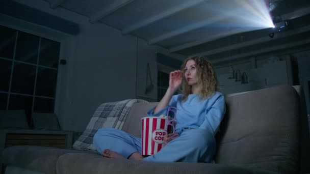 年轻的高加索女人在家里的放映机上看悲伤的3D电影 情绪化的女人坐在沙发上吃爆米花 高质量的4K镜头 — 图库视频影像