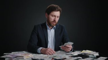Takım elbiseli bir adam yere düşürmeden önce bir yığın parayı ve birkaç banknotu karşılaştırıyor. Hayal kırıklığına uğramış görünüyor. Adam siyah odada yatıyor. Yüksek kalite 4k görüntü 