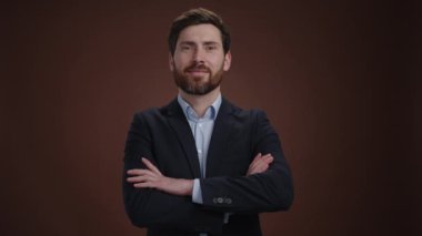 Takım elbiseli bir adam kollarını kavuşturup gülümseyerek kameraya bakıyor. Güzel giyinmiş ve çok mutlu görünüyor. O, kahverengi bir arka plandadır. Yüksek kalite 4k görüntü