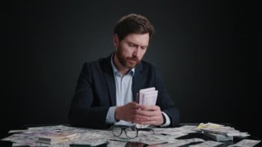 Takım elbiseli bir adam gözlük takmadan önce yığınla para sayıyor. Yorgun görünüyor. Adam siyah odada yatıyor. Bir yığın daha topluyor. Yüksek kalite 4K görüntü. 