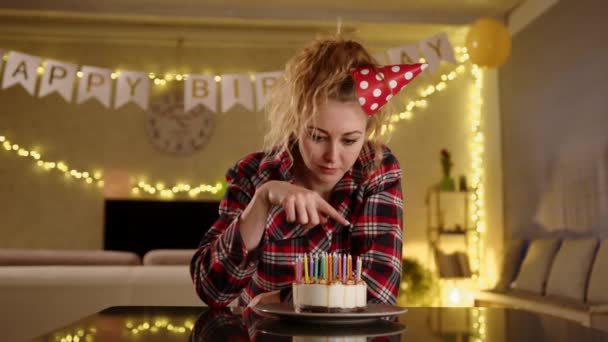 明るい笑顔でケーキの上にろうそくを数える誕生日キャップの女性 彼女は幸せそうだ ケーキの上のろうそくを別のろうそくに置き換えた 高品質4K映像 — ストック動画