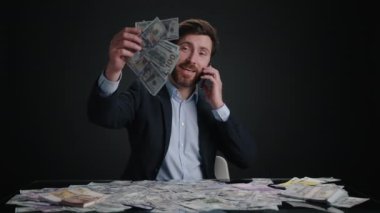 Takım elbiseli bir adam telefonda biriyle konuşurken para bırakıyor. Mutlu görünüyor. Adam siyah odada yatıyor. M, oney büyük bir yığın içinde. Yüksek kalite 4k görüntü 