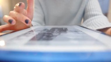 Manikürlü kadın elleri bilgileri tarıyor, özellikle tabletteki resimleri. Tabletteki resimlerin bulanık arkaplanı hızla değişiyor. Yüksek kalite 4k görüntü