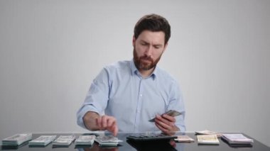 Mavi gömlekli bir adam para sayıyor ve doğru raflara koyuyor. Odaklanmış görünüyor. Adam açık gri bir odada. Yüksek kalite 4k görüntü 