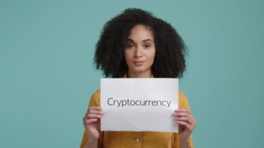 Esmer kadın, gündelik giysiler içinde elinde kripto para sözcüğüyle beyaz bir kağıt tutuyor. Kripto yatırımı reklamı yapan bir kızın portresi. Yüksek kalite 4k görüntü