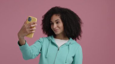 Güzel bir kadın pembe arkaplanlı selfie portresi yapıyor. Kıvırcık saçlı bir kızın yakın çekim görüntüsü. Yüksek kalite 4k görüntü