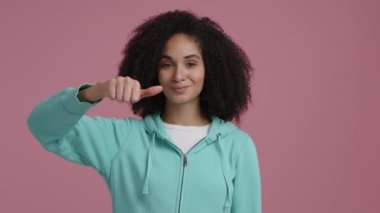 Koyu tenli kadın mutlu görünüyor ve başparmağını kaldırıyor. İyimser ve neşeli görünen çekici genç kıza yakından bak. Yüksek kalite 4k görüntü