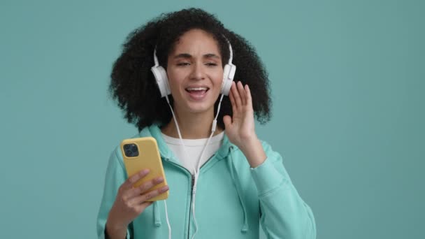 快乐的女孩 卷曲的 民族的头发 听着音乐和歌唱 一个快乐的 跳舞的女人 戴着白色耳机的画像 高质量的4K镜头 — 图库视频影像