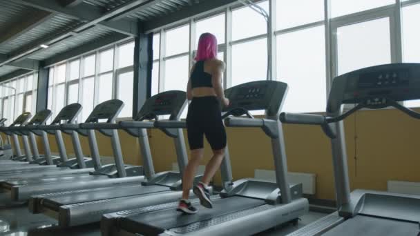 ウクライナのキエフ 2022年9月 ピンクの髪のジョギングだけで屋内でアクティブな女性 フィットネスジムでトレッドミル上で実行されているスポーティ女性アスリートのバックビュー 高品質4K映像 — ストック動画