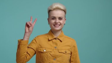 Yüzünde olumlu ifade olan mutlu bir kadının portresi. 30 'lu yaşlarda beyaz bir kızın zafer işaretini parmaklarıyla gösterdiği yakın çekim. Yüksek kalite 4k görüntü