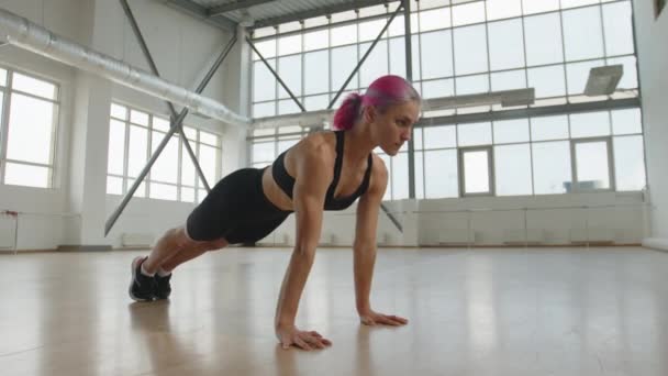 健康的30多岁的女孩独自在明亮的工作室里接受训练 粉红头发的年轻女子在剧烈运动时做俯卧撑 高质量的4K镜头 — 图库视频影像