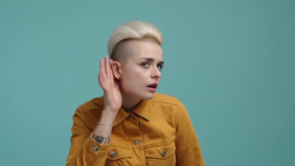 若い女性の映像は彼女の耳を開いておく 魅力的な 若い女性が孤立した青の背景を持つ音に耳を傾ける 高品質4K映像 — ストック動画