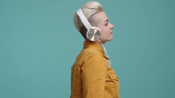 一个戴着白色耳机的时髦 跳舞的女孩的画像 兴高采烈的年轻女子穿着黄色休闲装 听着网上流淌的音乐 高质量的4K镜头 — 图库视频影像