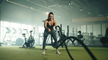İyi yapılı, tatlı bir kadın spor salonunda çapraz formda bir ip üzerinde egzersiz yapıyor. Geniş bir oda, elektrikli aletler, kardiyo makineleri, arka planda büyük bir ayna. Yüksek kalite 4k görüntü