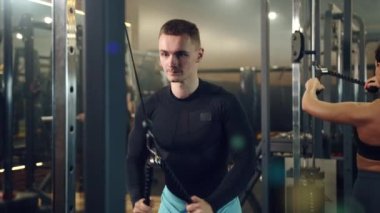 Spor salonundaki dikey sıra makinesinde egzersiz yapan yakışıklı adamın orta boy fotoğrafı. Sırt egzersizi. Spor malzemeleri, arka planda kadın ve erkek eğitimi. ve yüksek kalite 4K görüntü