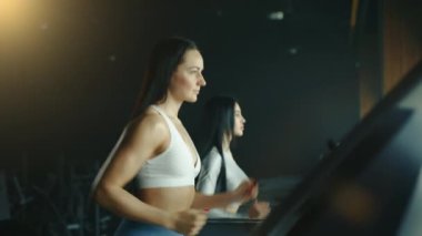 İri yapılı, kahverengi saçlı iki genç kadının koşu bandında koşup düz bakışlarının yarı uzunluğunda. Kas ve sırt kaslarına odaklan. Yüksek kalite 4k görüntü