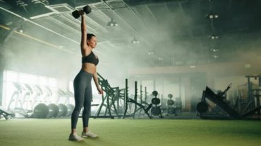 Atletik genç kadın spor salonunda dambıl egzersizi yapıyor. Kadın tek kollu dambıl kapıp kollarını değiştiriyor. Sisli arka plan, kardiyo alanı. Yüksek kalite 4k görüntü
