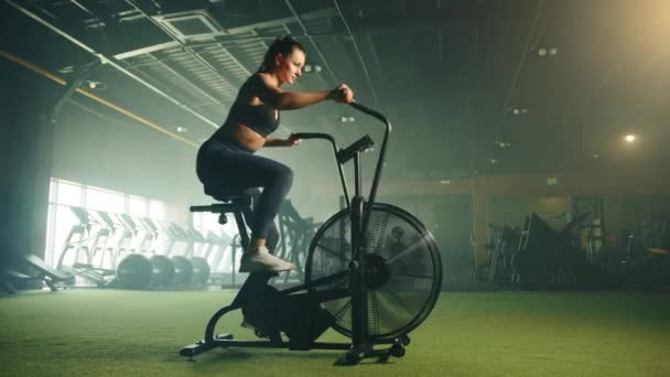 年轻健康可爱的女子正在全副武装的健身房接受空中自行车训练 马尾辫的女人 汗流浃背的身体穿着运动上衣和腿 高质量的4K镜头 — 图库视频影像
