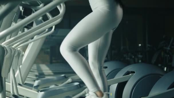 年轻美丽的棕色头发的健康的身体女人穿着银色运动上衣和腿练习椭圆教练在健身房 一排椭圆形的训练员 高质量的4K镜头 — 图库视频影像