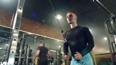 Dikey sıra makinesi, eller ve sırt egzersizleri yapan yakışıklı bir genç. Spor tesisleri, arka planda spor yapan kadın, erkek. Yüksek kalite 4k görüntü