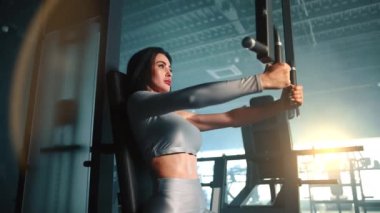 Tam teçhizatlı spor salonunda göğüs sineği makinesi üzerinde egzersiz yapan atletik genç bir kadın. Orta boy. Gümüş spor tişörtü ve kaslı kollar içinde terli bir vücut. Yüksek kalite 4k görüntü