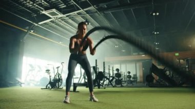 Geniş spor salonunda dar spor giyim egzersizleri yapan hoş ve formda genç bir kadın. Tam atış. Arka planda koşu bantları olan geniş bir kardiyo alanı. Yüksek kalite 4k görüntü