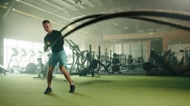 Modern kardiyo alanında sporcu genç ve yakışıklı bir adam tarafından yapılan savaş halatı üzerinde Grappler fırlatma egzersizi. Adamın uzun kollu sıkıştırma gömleği ve şortu var. Yüksek kalite 4k görüntü