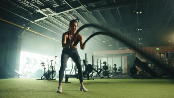 広々としたジムでの戦闘ロープとスキンタイトなスポーツウェアの演習でかわいい若いフィット女性 フルショット 背景にトレッドミル付きの大きな心臓領域 高品質4K映像 — ストック動画