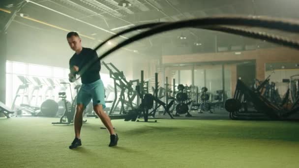 采集器抛掷运动的战斗绳 由运动年轻英俊的男子在健身房与现代有氧区域 男人有长袖压缩衬衫 高质量的4K镜头 — 图库视频影像