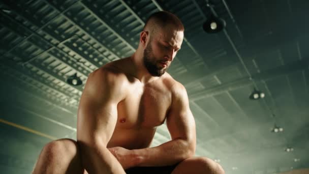 裸体の胴座ってダンベルを持ち上げる運動青年の中型クローズアップ 男は真剣に見えると彼の足を構築することに焦点を当て 腕のトレーニング 高品質4K映像 — ストック動画