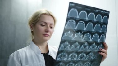 Sarışın doktorun MRI 'ı iyice incelediği orta ölçekli bir görüntüsü. Laboratuvar önlüklü hoş bir kadın MR sonuçlarını elinde tutuyor ve şaşırmış görünüyor. Beyaz arka plan. Yüksek kalite 4k görüntü