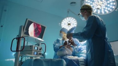 Genç cerrah ve hemşire tıbbi monitöre bakarak estetik ameliyat yapıyorlar. Modern ekipmanlar, arka planda yüksek kaliteli ışıklandırma. Yüksek kalite 4k görüntü