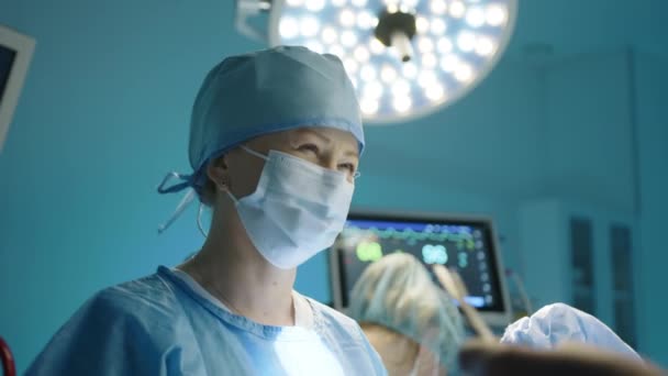 整形手术过程中 微笑的女护士的中等近视 医护人员领着手术室的灯光在后台进行监控高质量的4K镜头 — 图库视频影像