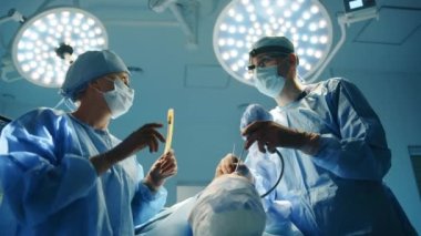 Cerrahi farlı ve güvenlik gözlüklü hemşire ve genç cerrah estetik ameliyat sırasında mesafeye bakıyor. Operasyon ışıkları. Yüksek kalite 4k görüntü