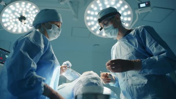 男性の整形外科医と看護師は手術室での整形手術手順について話し合います 患者はテーブルの上にいる 主演の演劇照明 高品質4K映像場合 — ストック動画